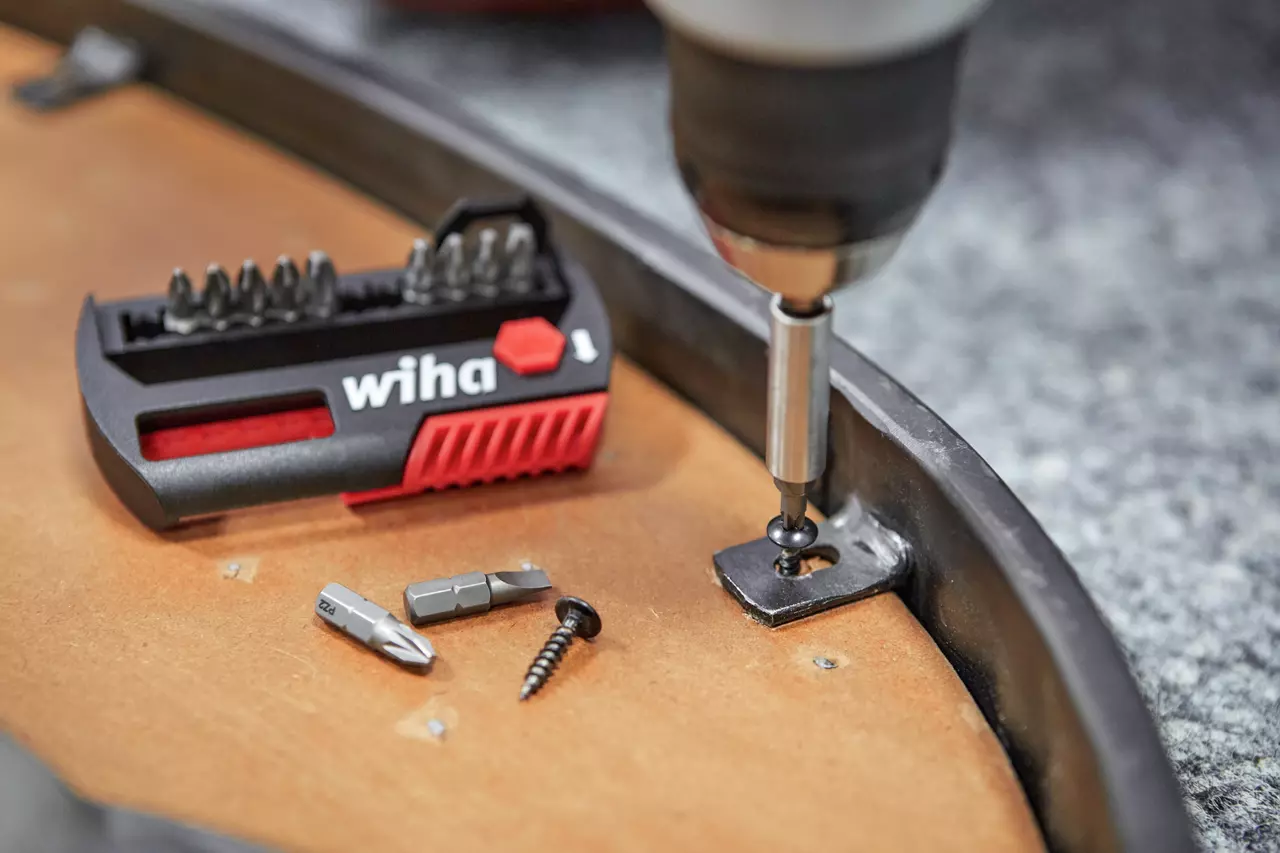 Electric screwdriver driving a screw into a metal bracket with a bit set nearby on a wooden surface.