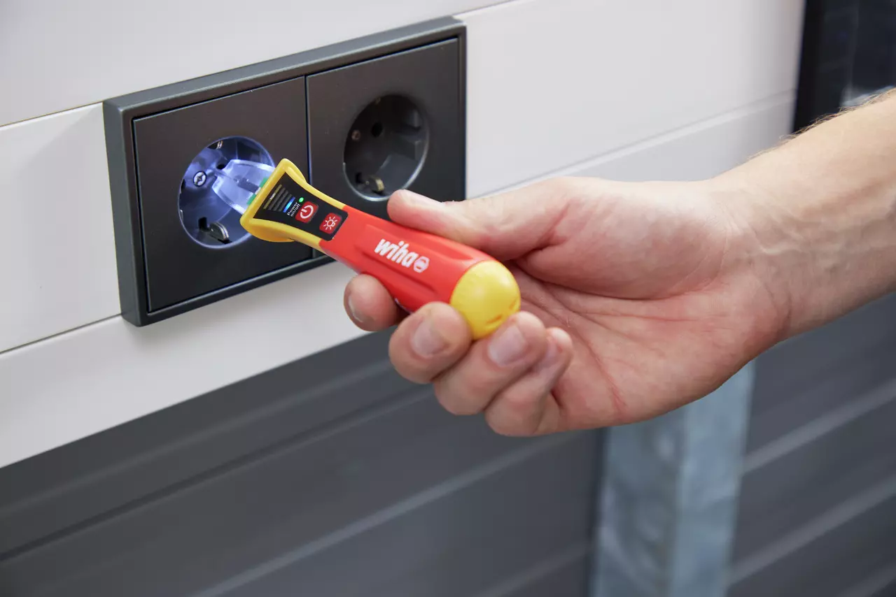 Hand using a non-contact voltage detector near an electrical socket