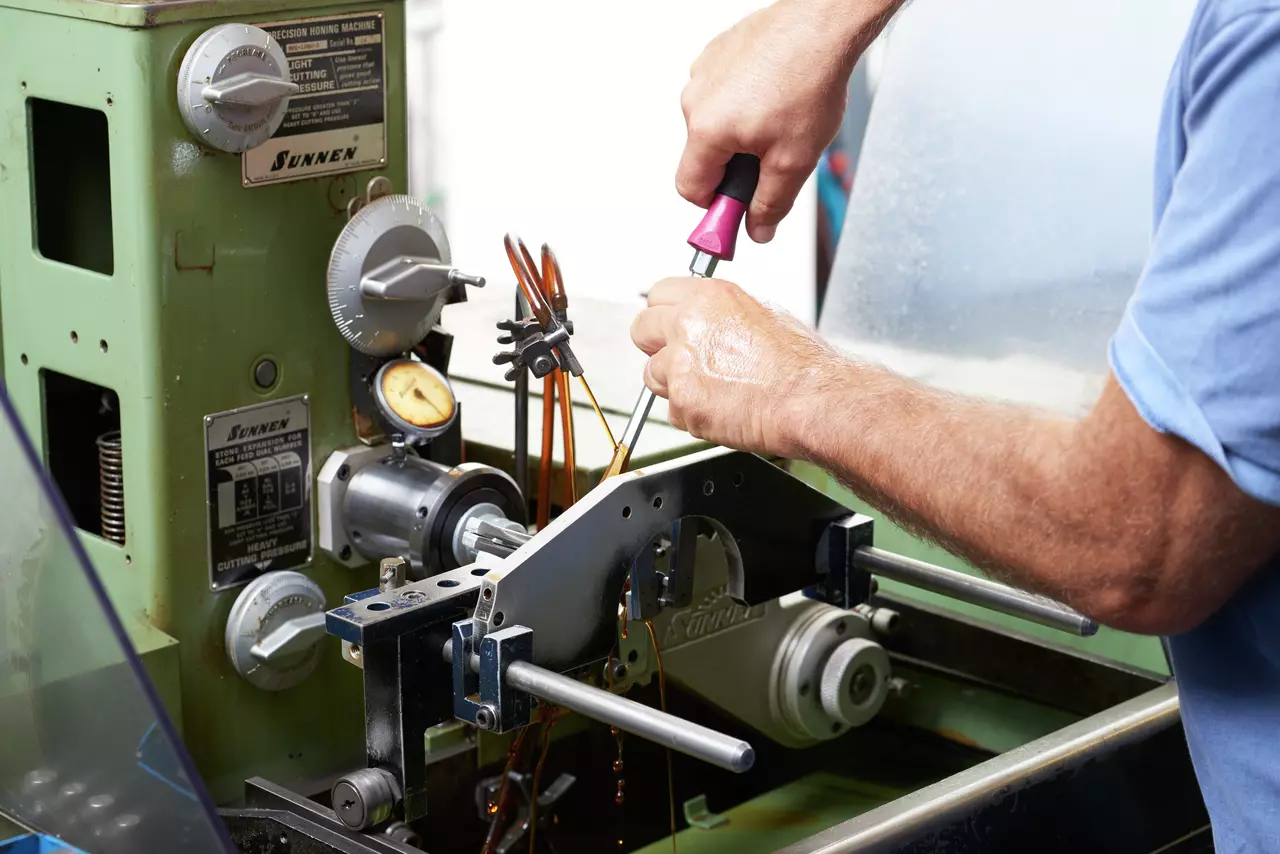 Person using a screwdriver on a green precision honing machine
