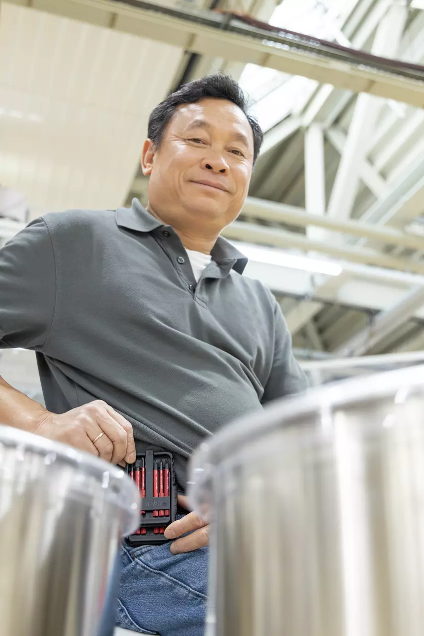 A person in an industrial setting with a screwdriver set on their hip.
