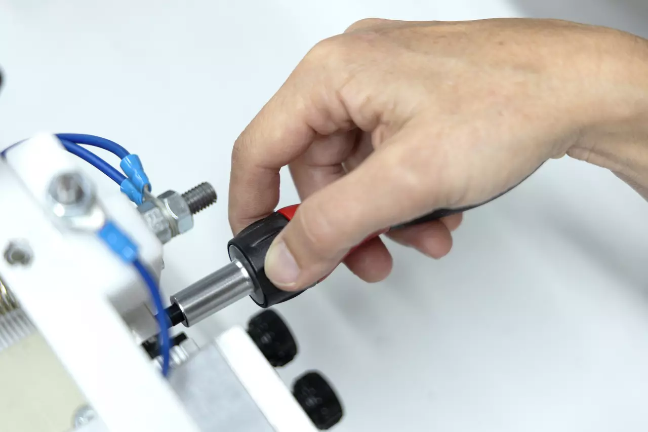 A hand using a ratchet screwdriver on a metal component with blue wires.