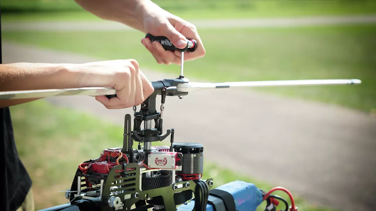 Person using a screwdriver to adjust a model helicopter rotor outdoors.