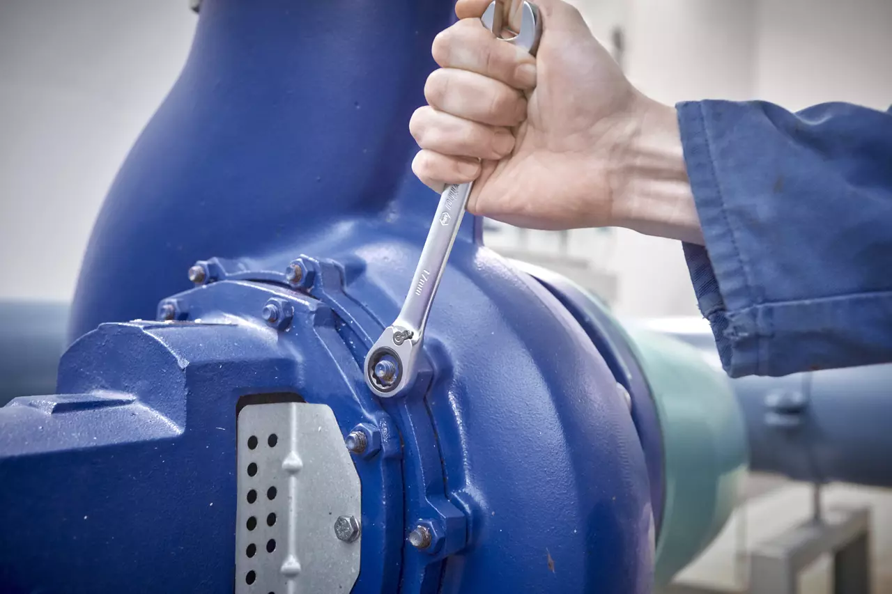 A person using a ratchet wrench on a large blue machine.
