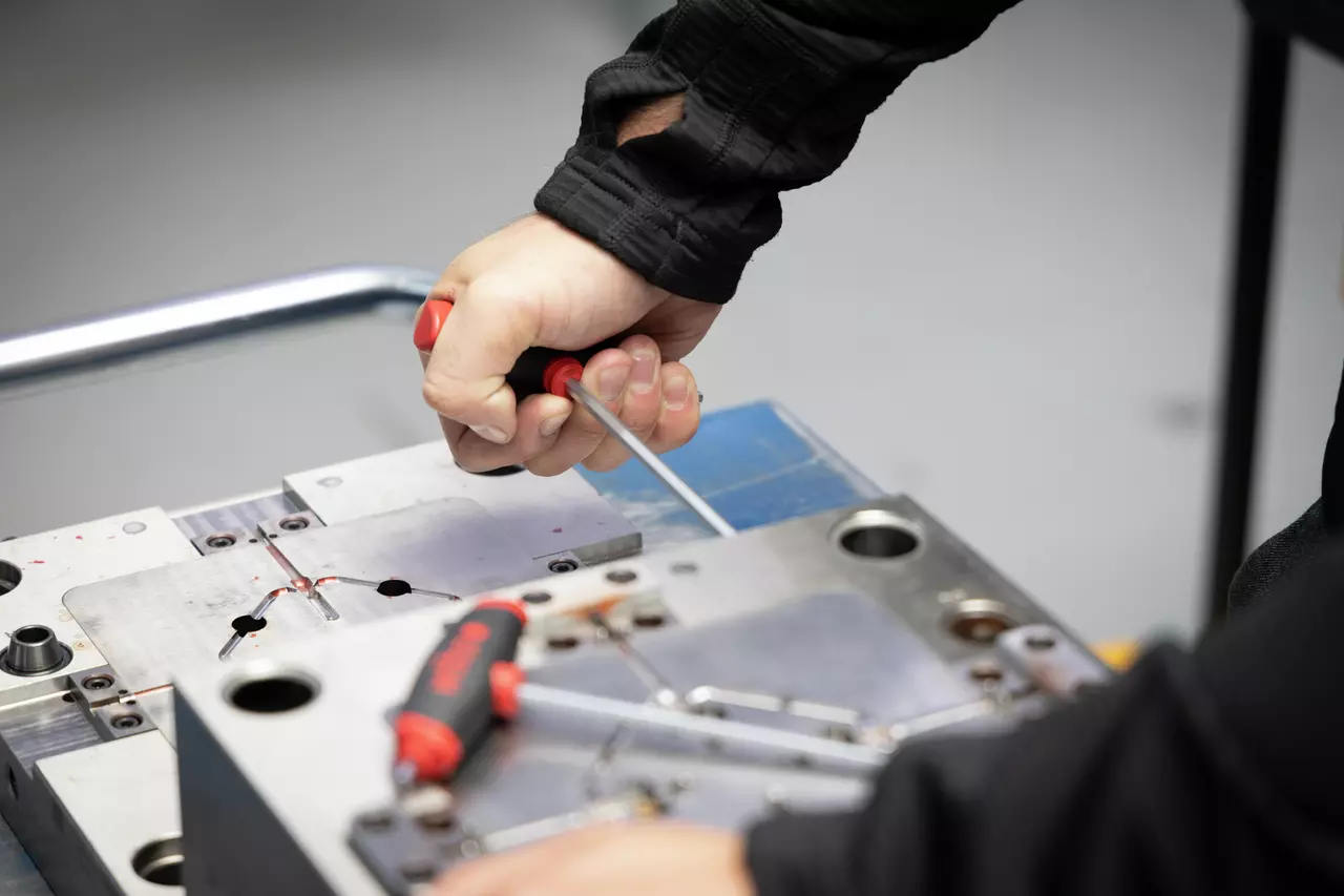 A person using a screwdriver on a metal surface, with another tool nearby.