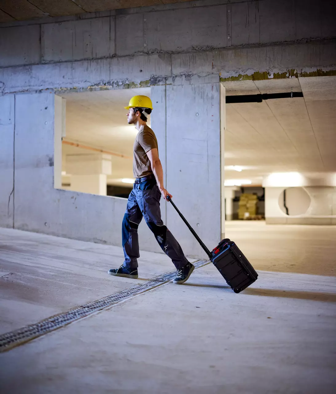 A person in a hard hat pulling a black trolley in a concrete building.
