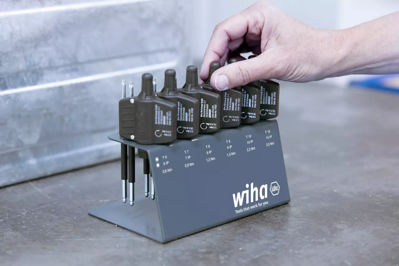 Hand holding a torque tool from a set on a metal stand with various sizes labeled