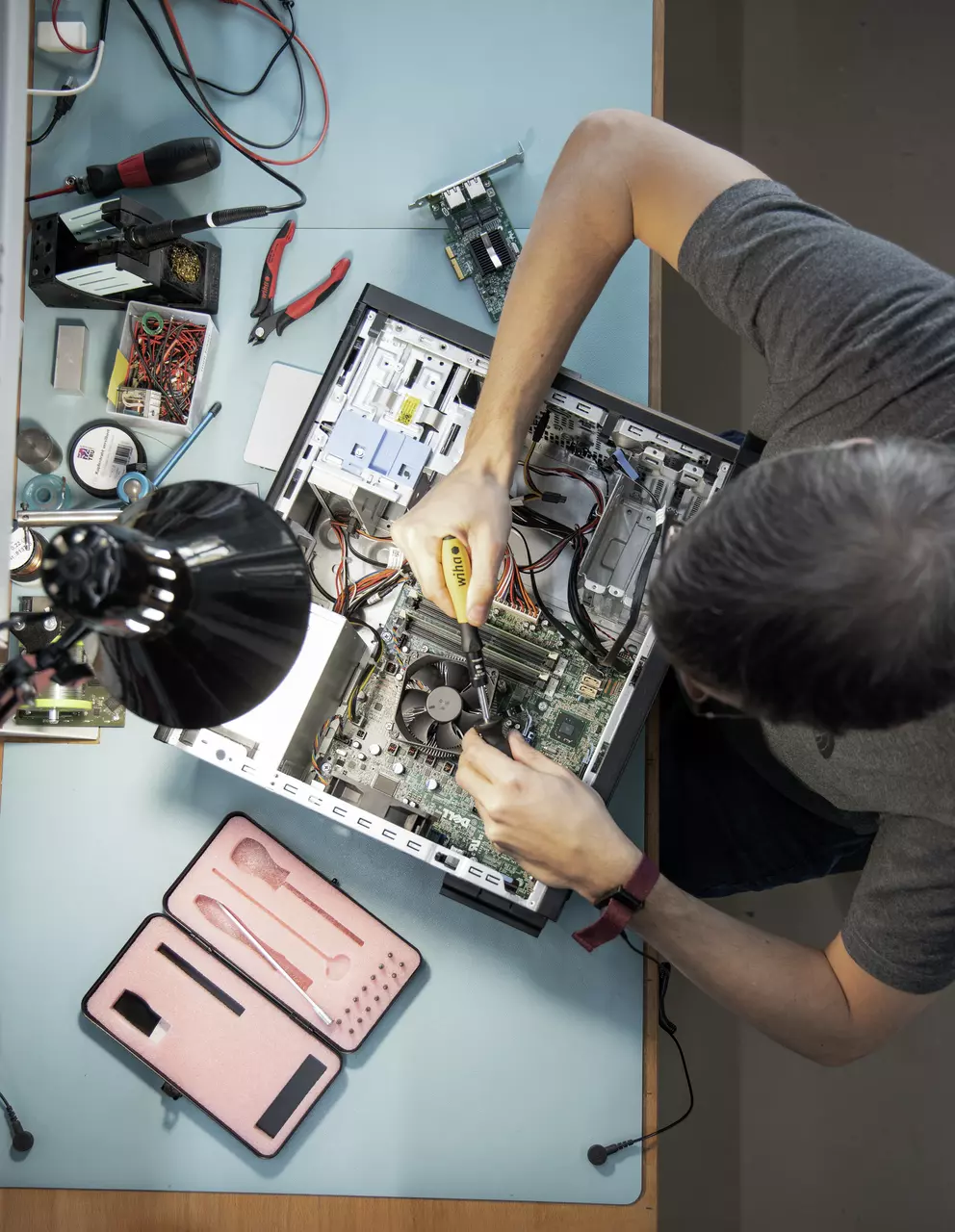 Personne utilisant un tournevis pour réparer un ordinateur ouvert sur un bureau avec des outils