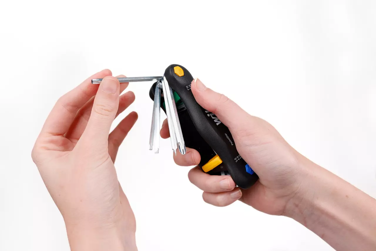 A hand holding a folding hex key set with various sizes extended.