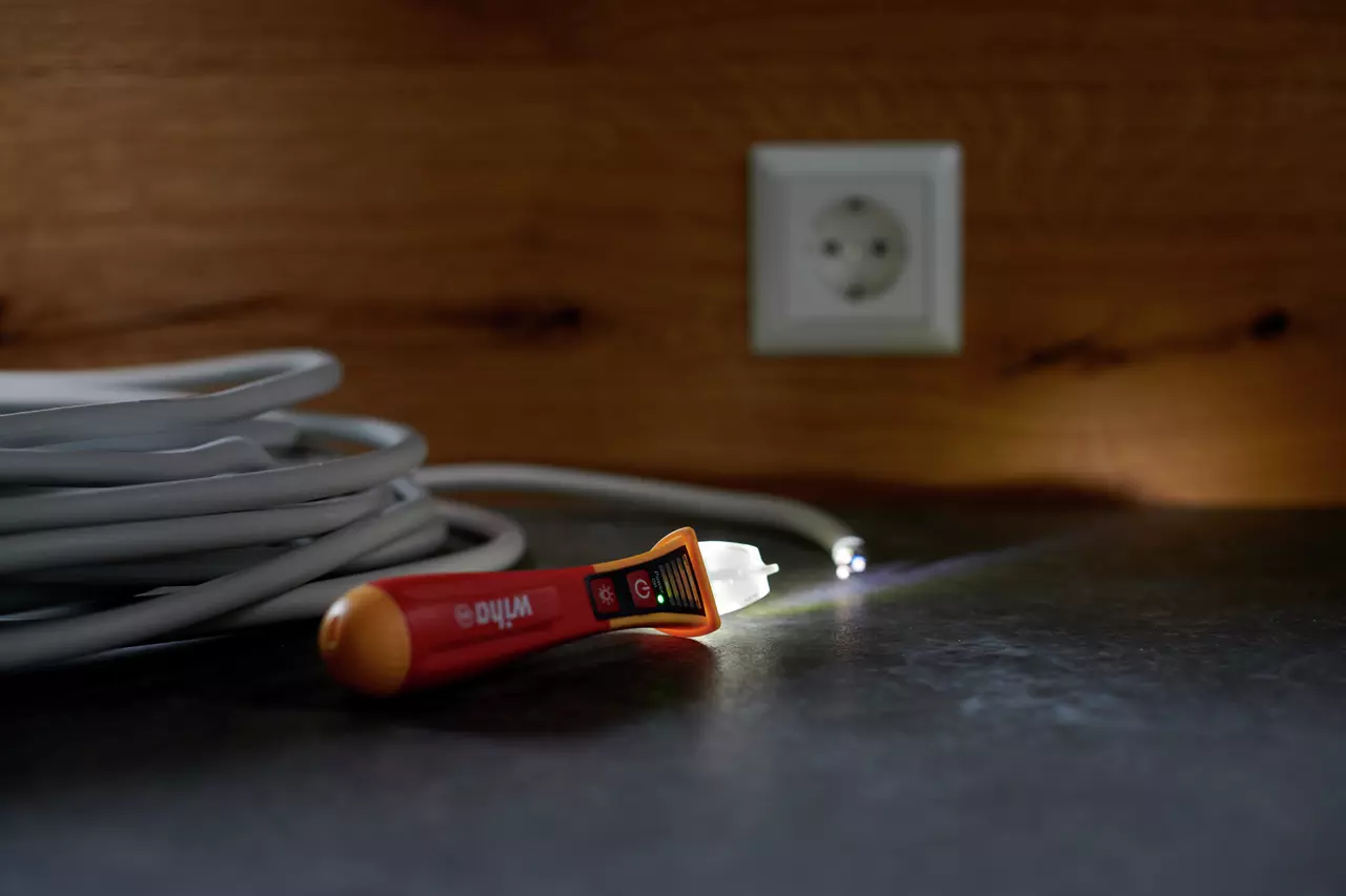 Non-contact voltage detector on table near coiled cable and wall socket.