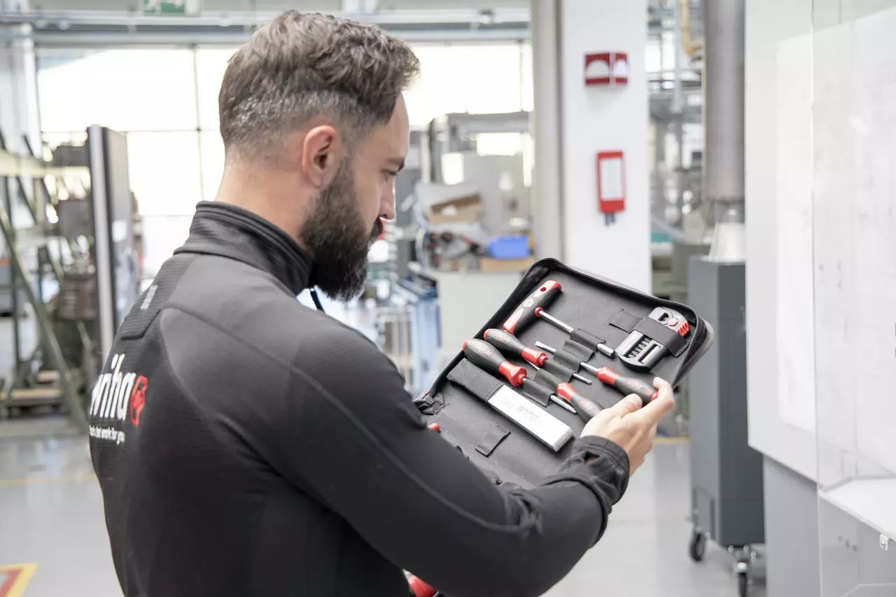 A person holding an open tool set case with various screwdrivers and tools inside, in a workshop setting.