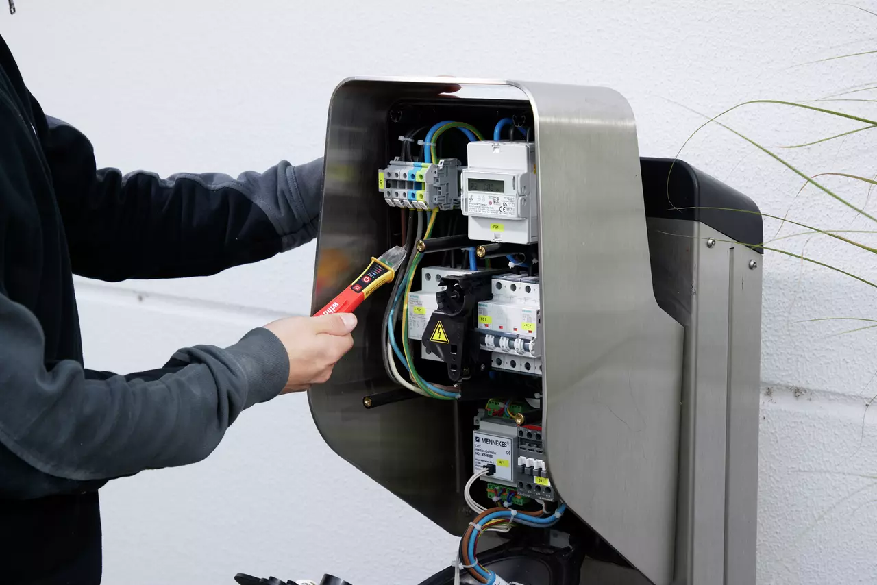 A person uses a non-contact voltage detector on an electrical panel with wires and circuit breakers.