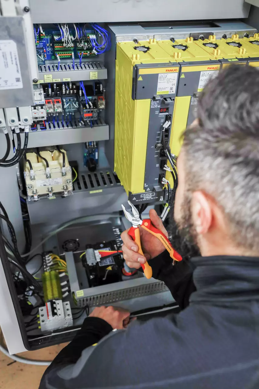 A person using combination pliers on electrical components in a control panel.