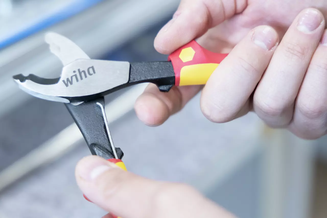 Person holding a red and yellow-handled cable cutter with black and silver blades.