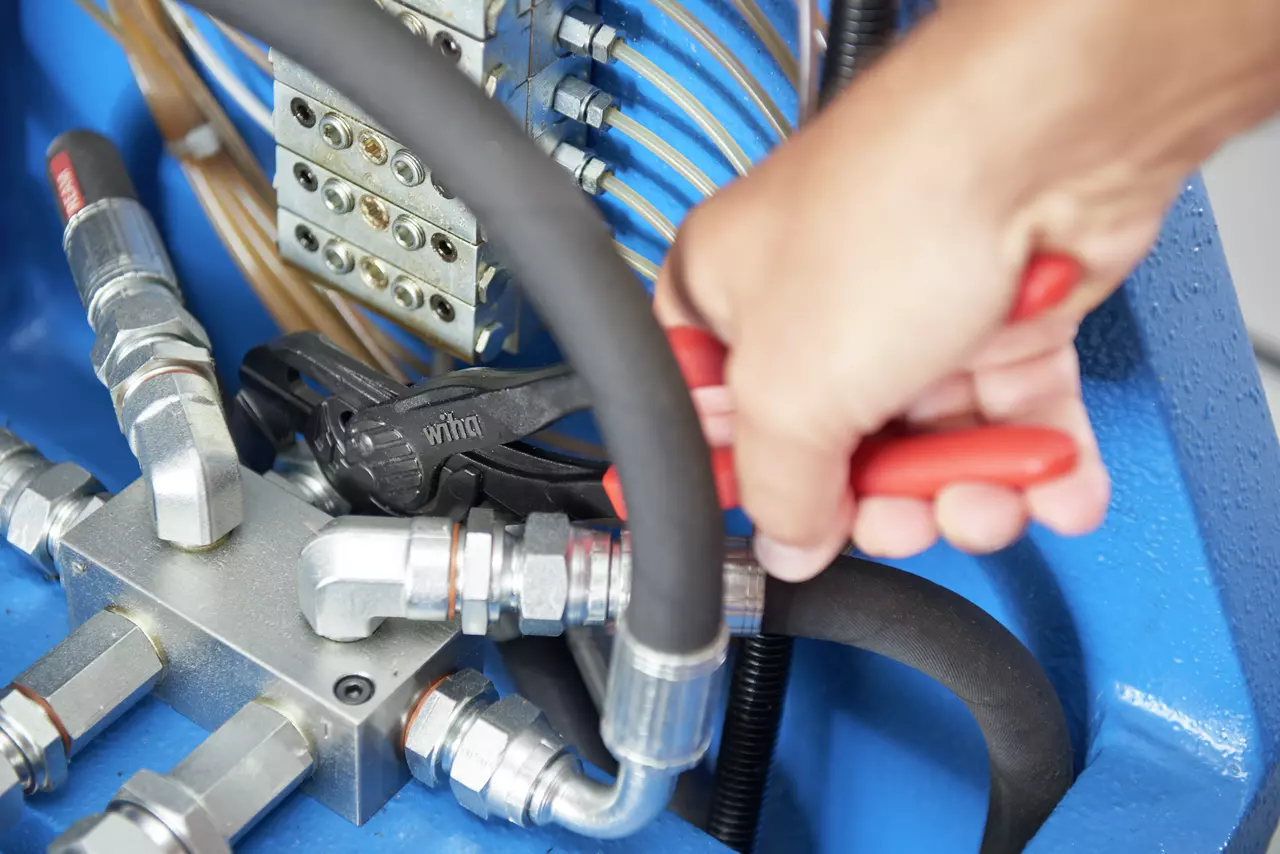 A person using a red-handled tool on metal pipes in a hydraulic system.