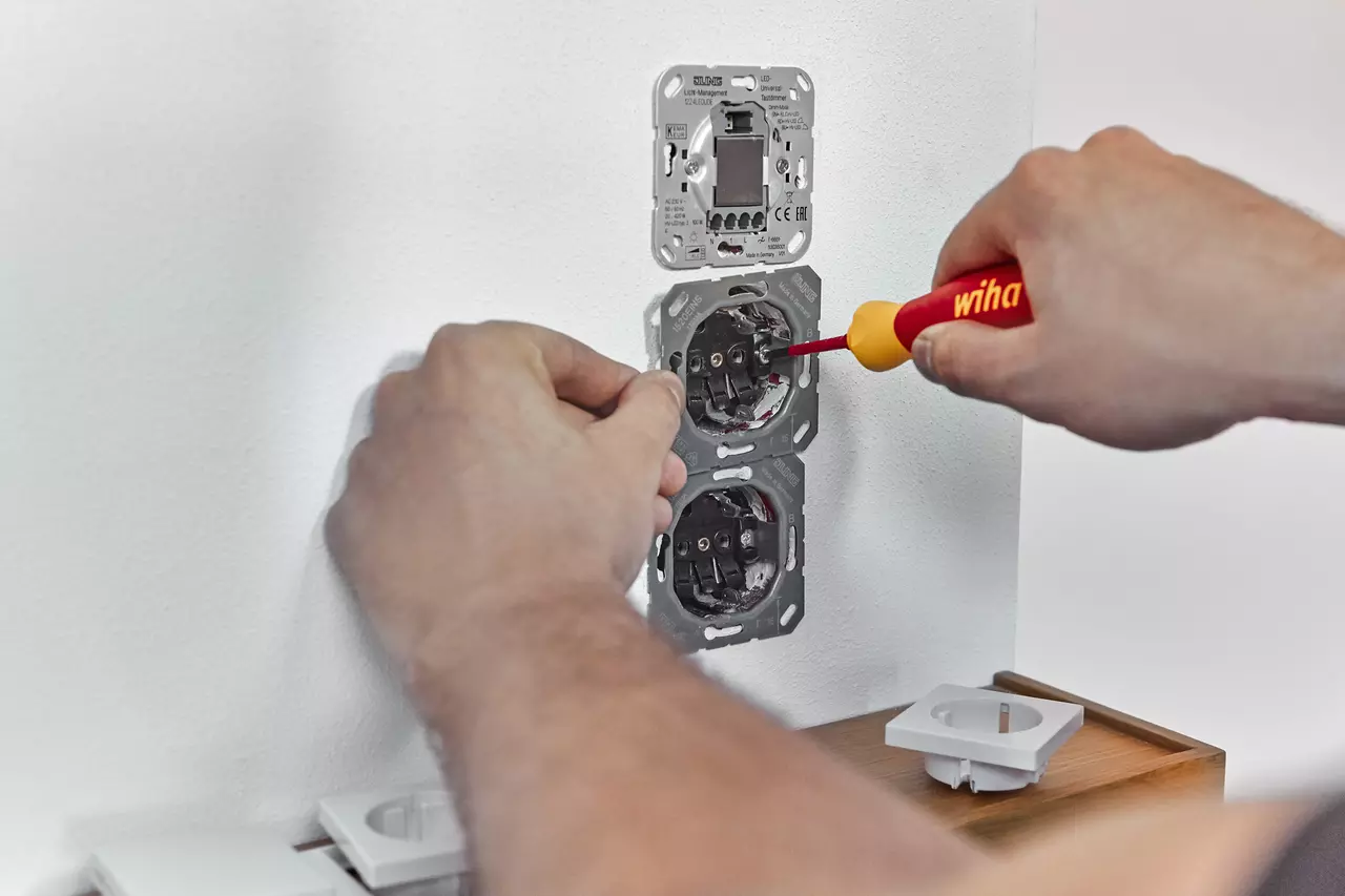 Person using a red and yellow screwdriver to install sockets in a wall