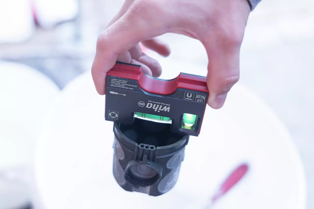 Person holding a pocket level with clamp, red and black, showing a green bubble vial.