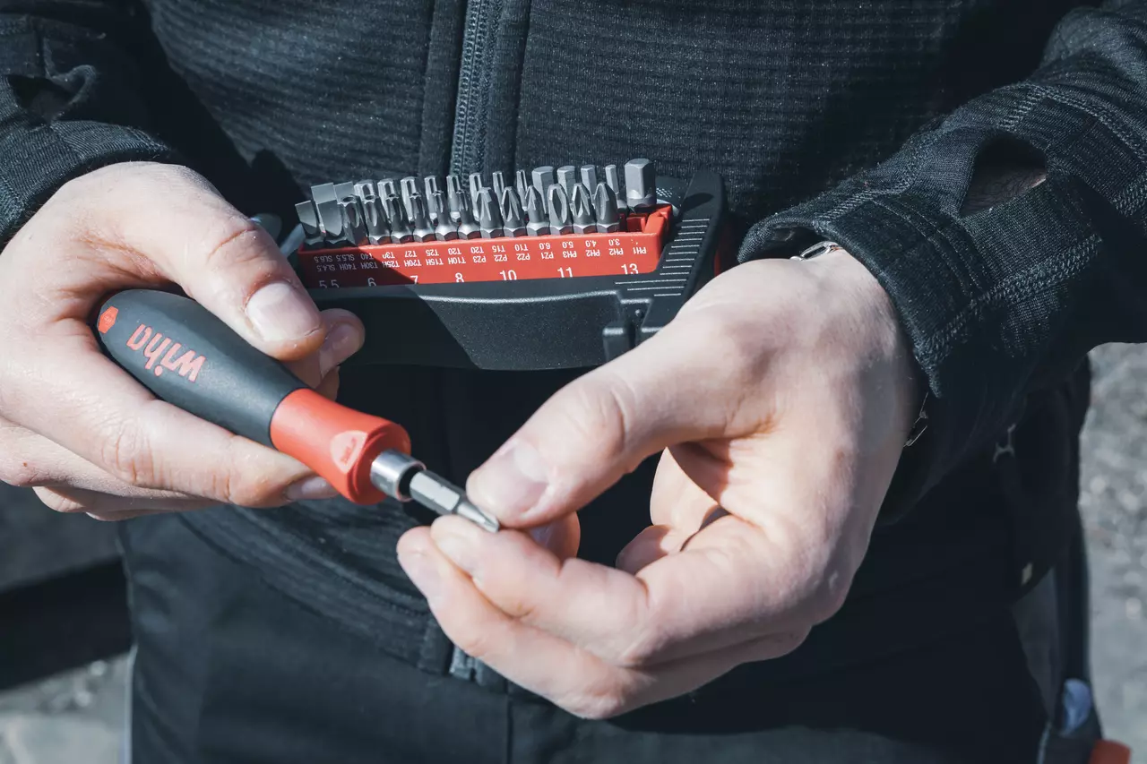 Person holding a screwdriver handle and a bit set in a black and red case