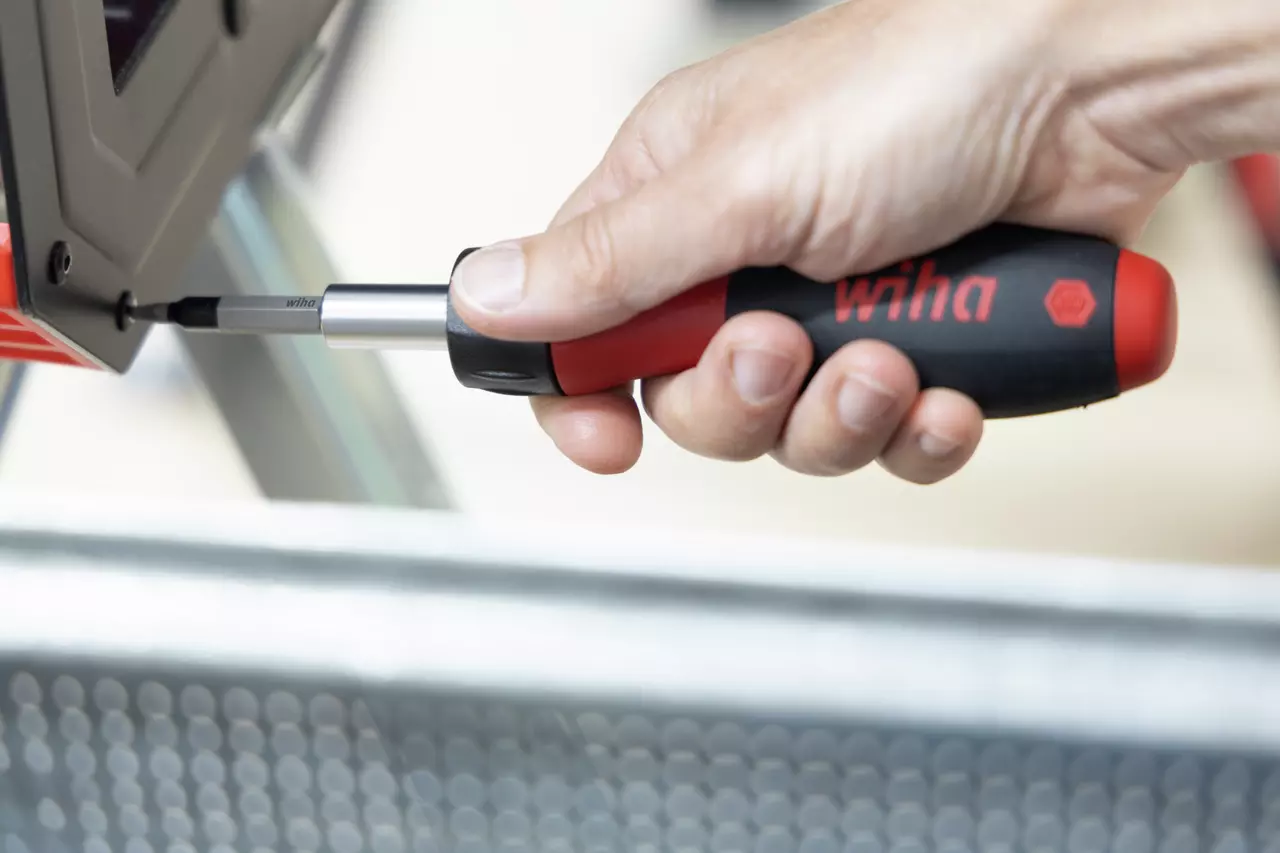 Hand using a red and black ratchet screwdriver on a screw