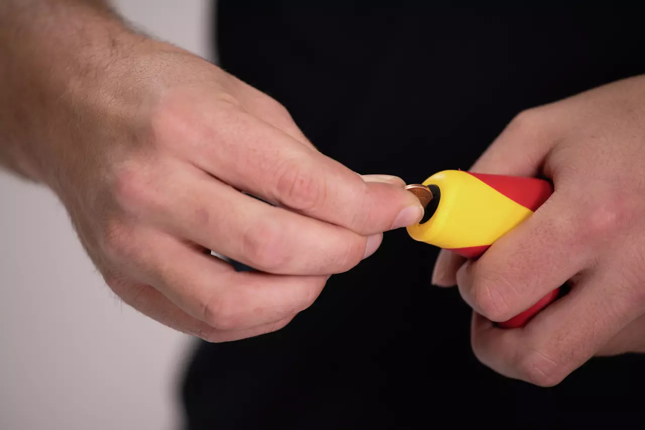 Person inserting a coin into the handle of a red and yellow tool.