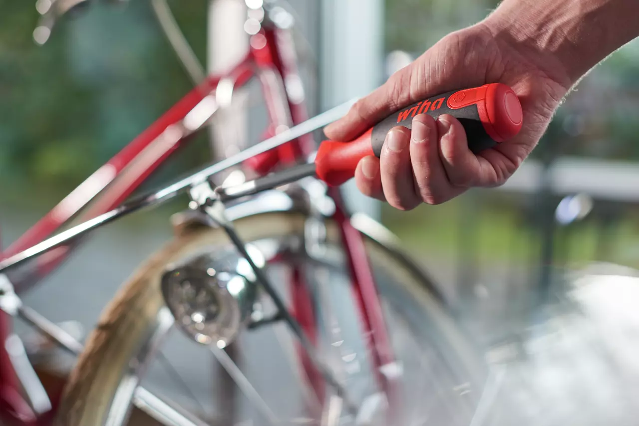 Hand using a screwdriver to adjust a red bicycle