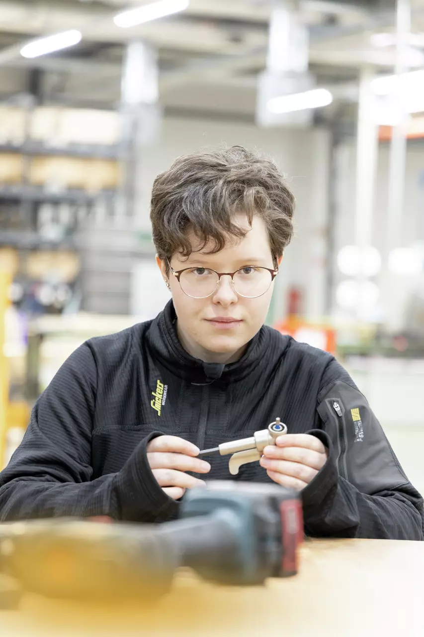 A person holding a small tool in their hands, sitting at a table in a workshop.