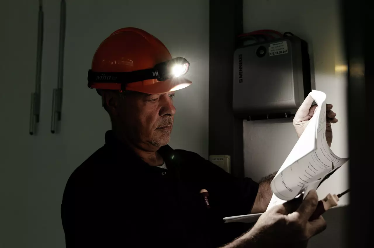 A person with a helmet and headlamp reads a document in a dark room.