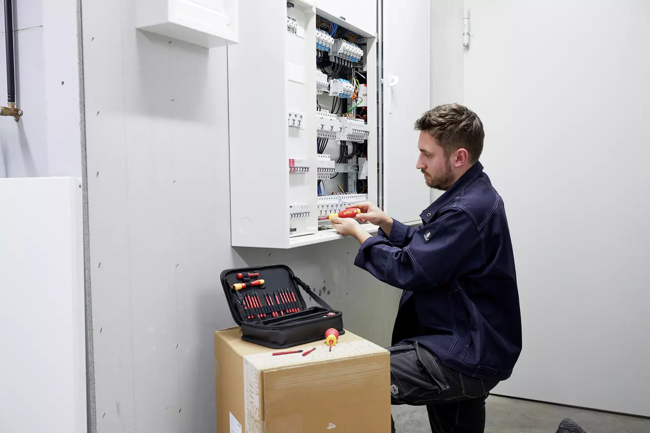 A person working on an electrical panel with a set of screwdrivers nearby.