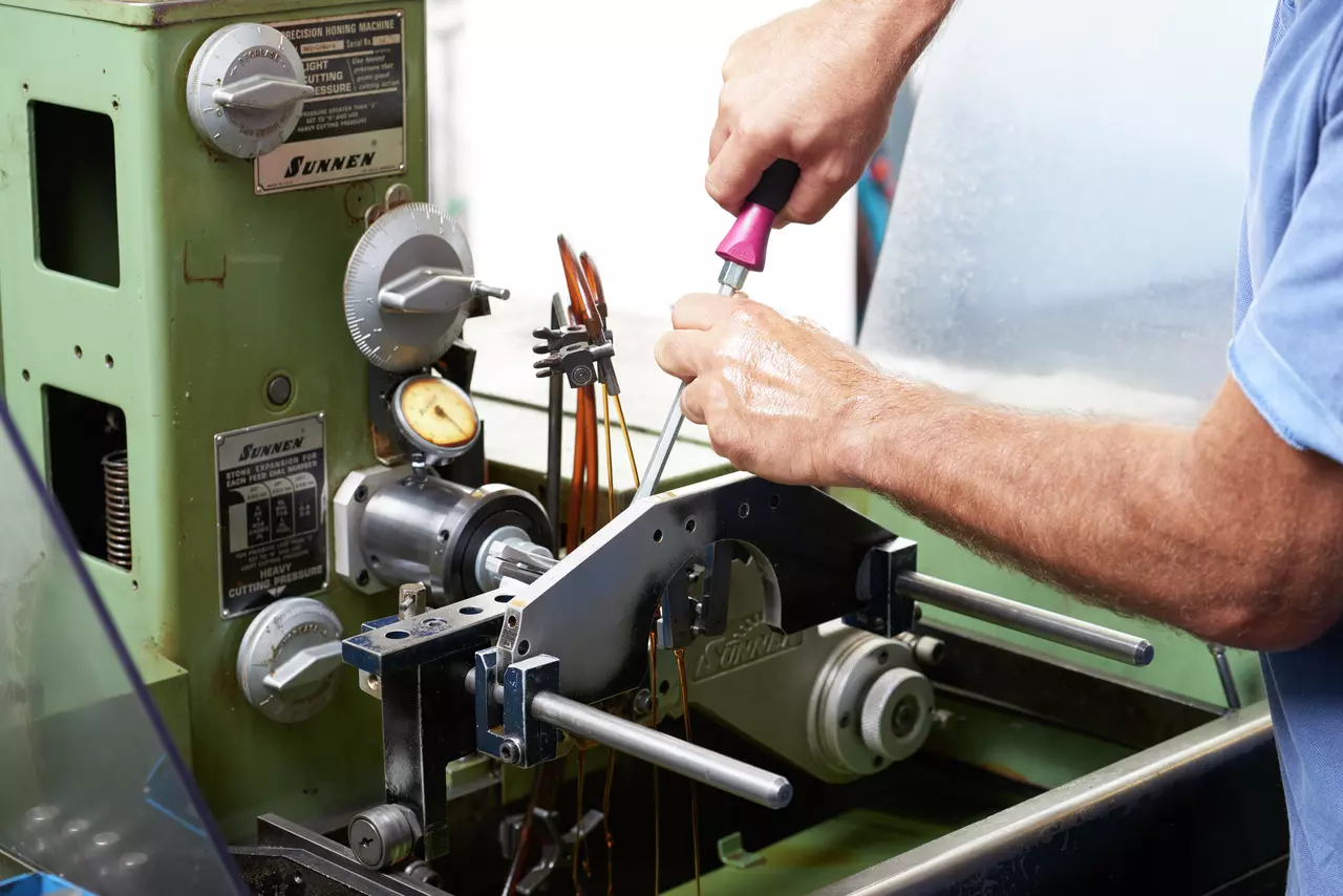 Person using screwdriver on a green precision honing machine.