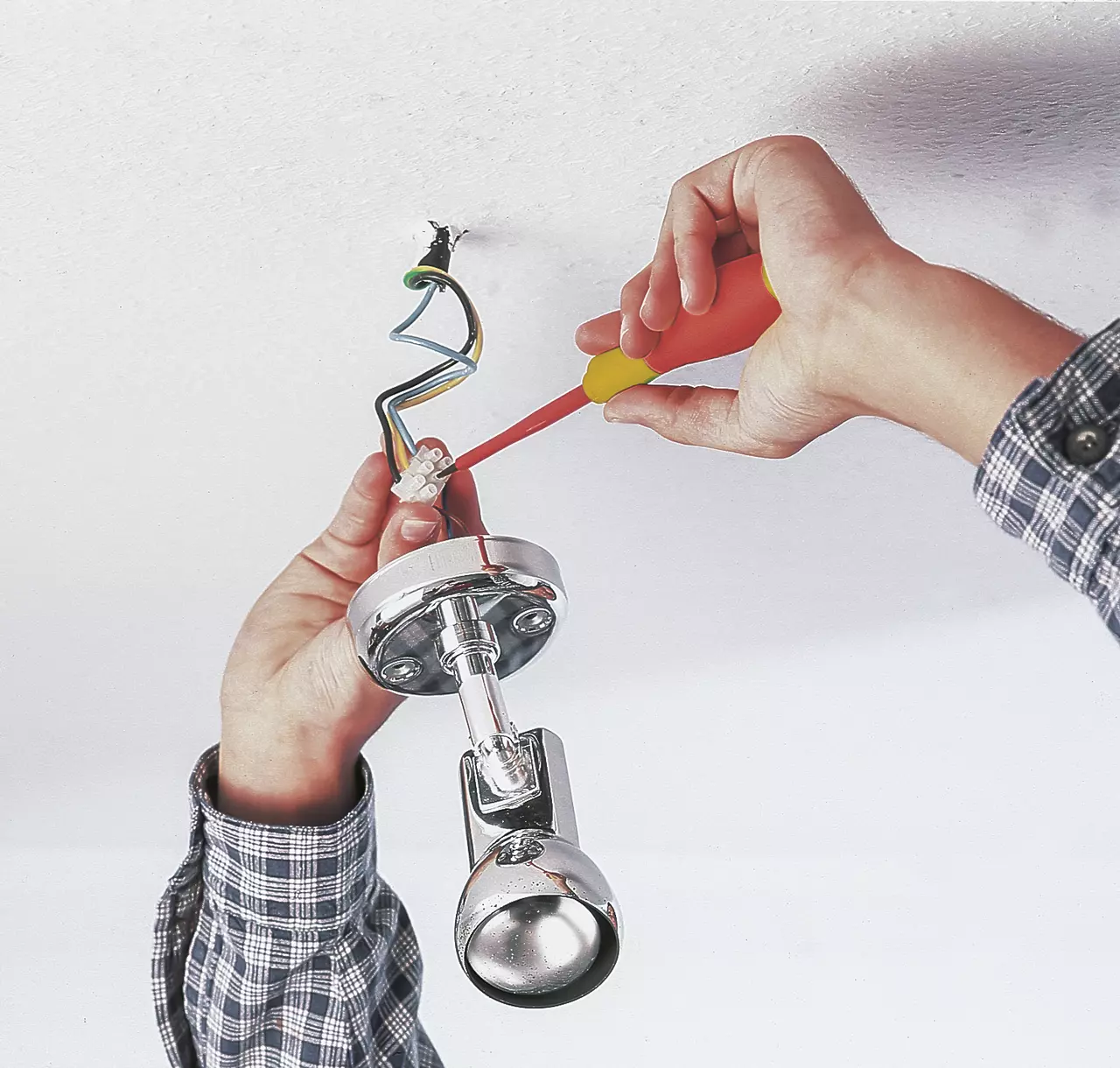 Person using an electrical screwdriver to install a ceiling light fixture.