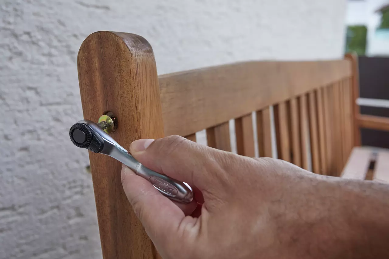 A person uses a ratchet wrench on a wooden bench