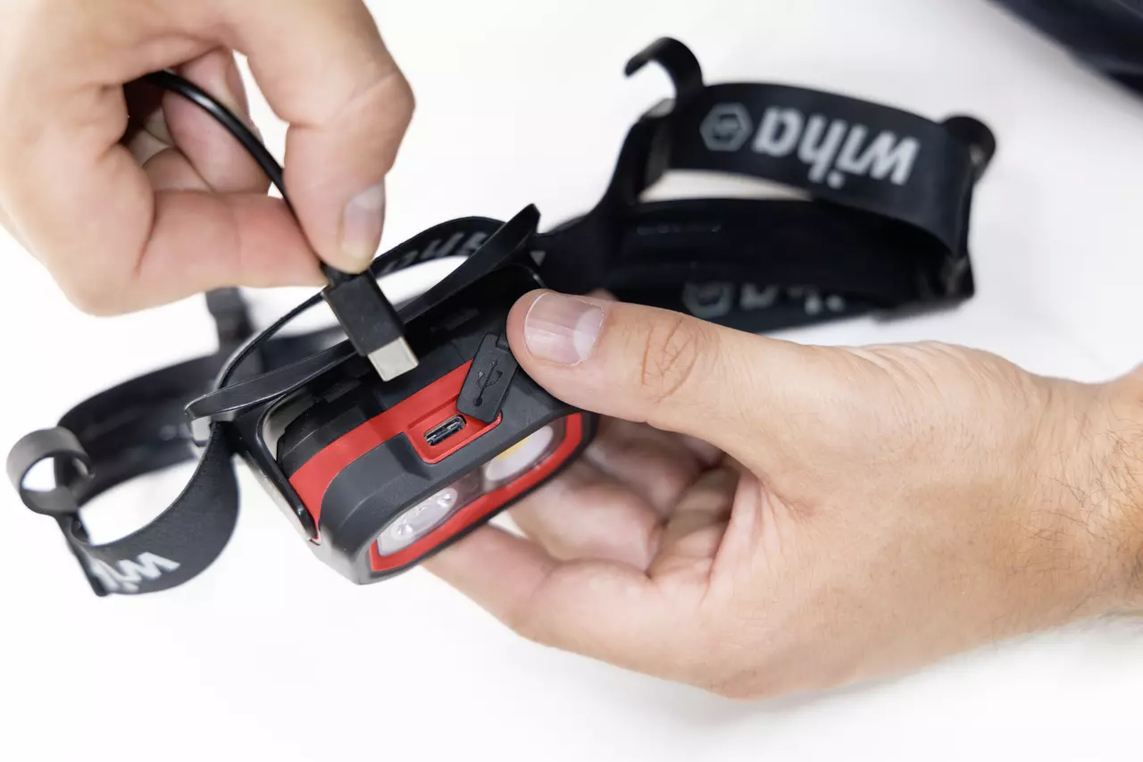 A person charging a headlamp with a USB cable.