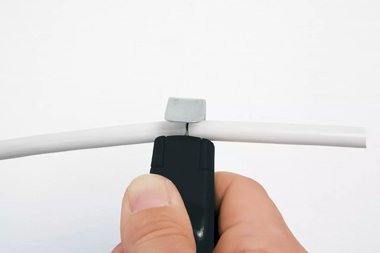 Hand holding a stripping tool working on a white cable.