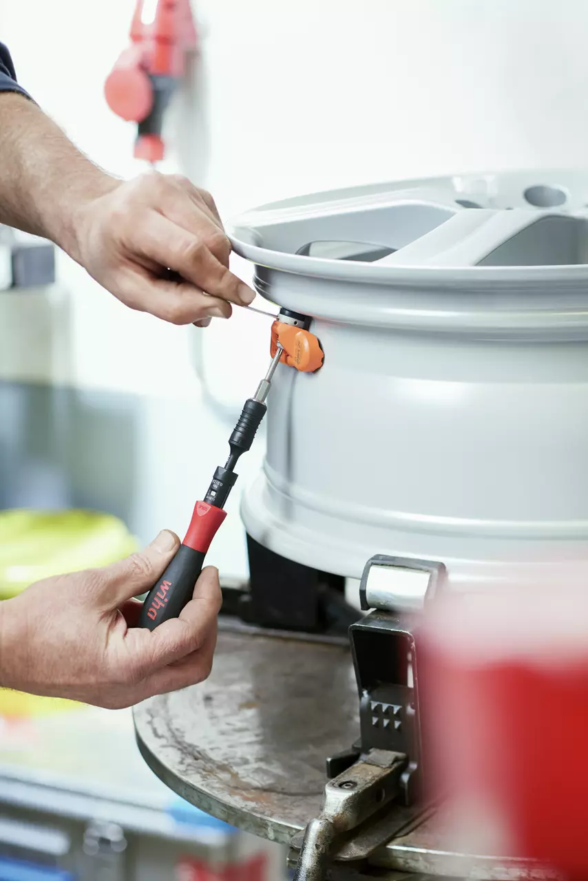 Person using a torque screwdriver on a silver wheel rim in a workshop.
