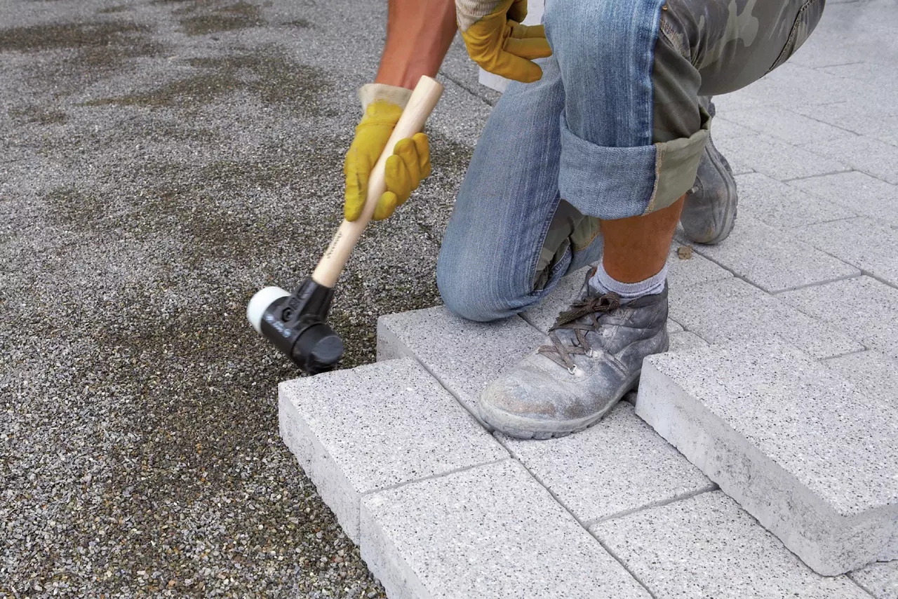Person using a rubber mallet to lay paving stones