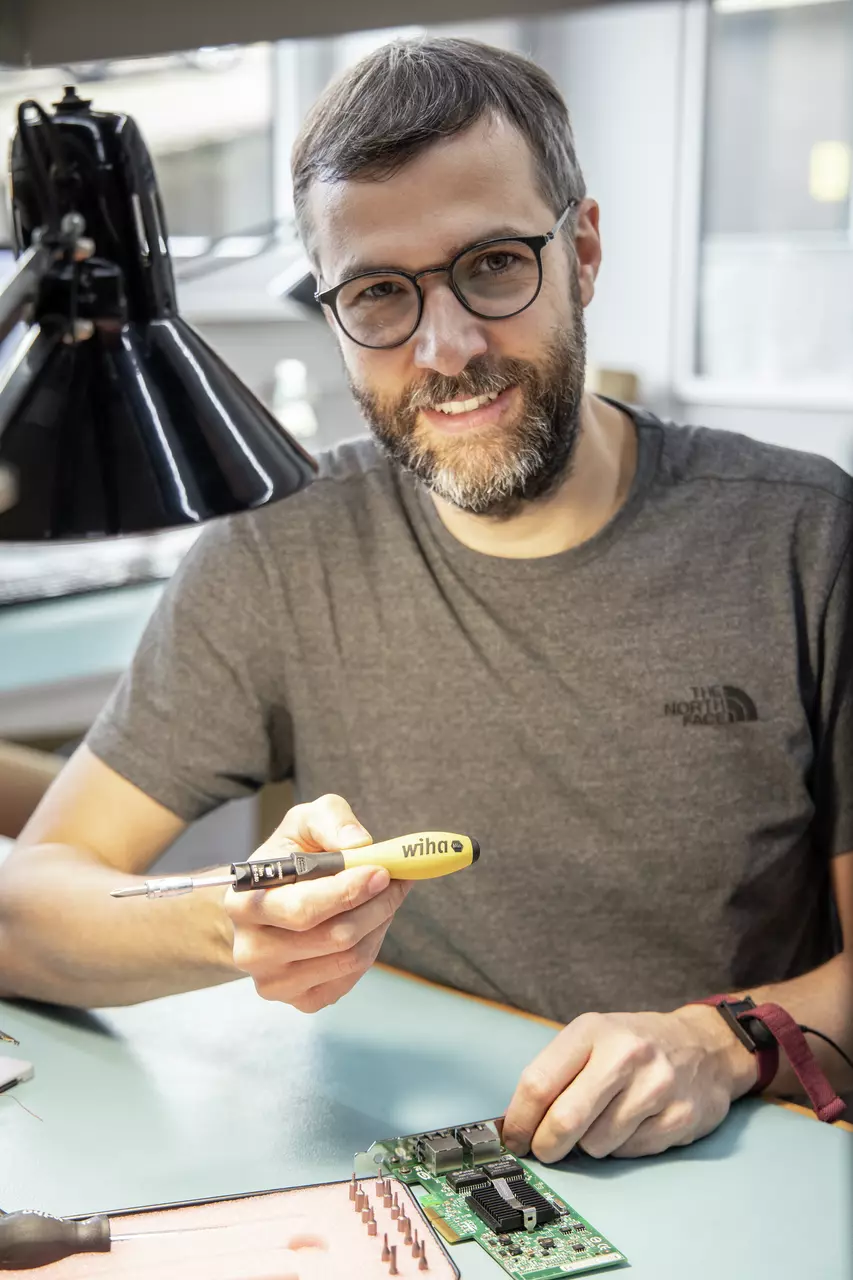 A person holding a yellow and black screwdriver, working on an electronic circuit board.
