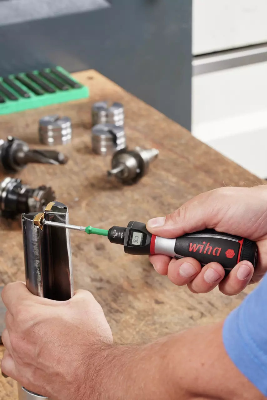 Person using a digital torque screwdriver on a metal object in a workshop.