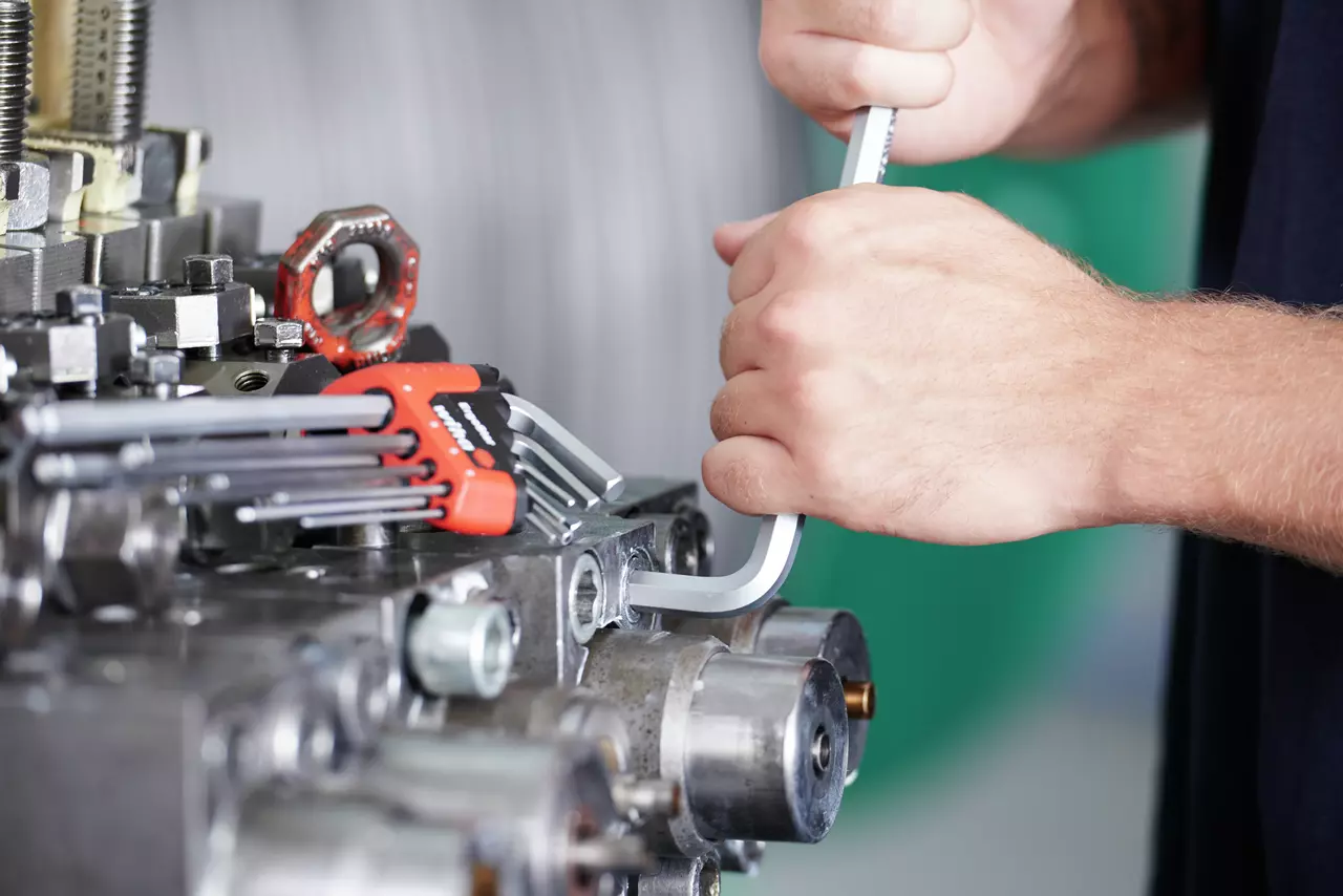 Person using a hex key on machinery with a set of hex keys nearby.
