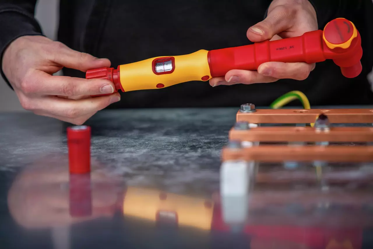 A person holds a red and yellow torque wrench near a metallic structure.