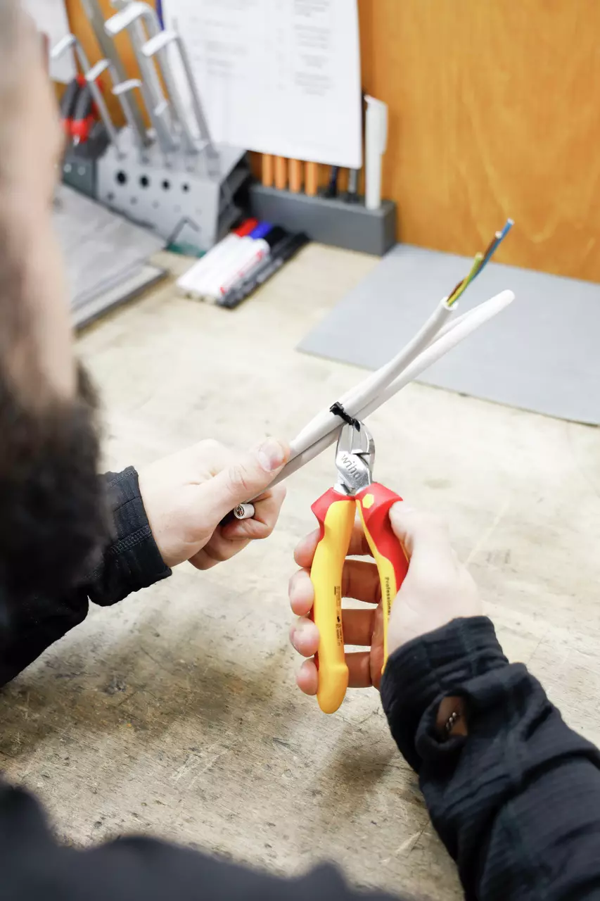Person cutting a cable tie with a diagonal cutter on a table.