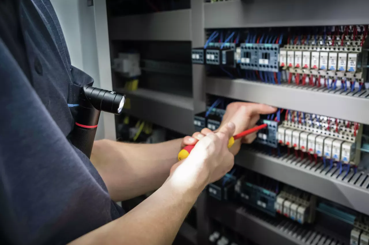 A person works on electrical panel with a screwdriver and flashlight.