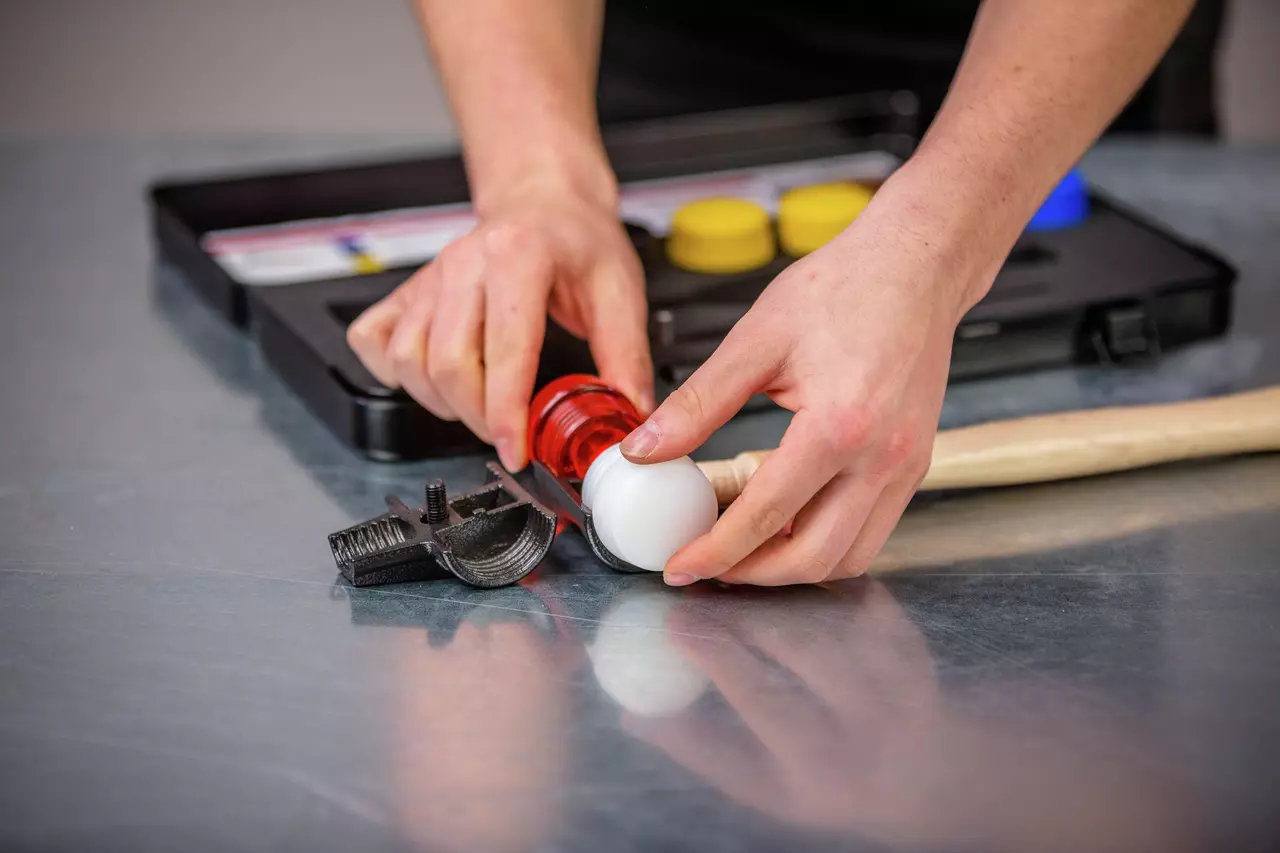 A person assembling a red and white mallet head on a wooden handle next to a toolbox on a metal surface.