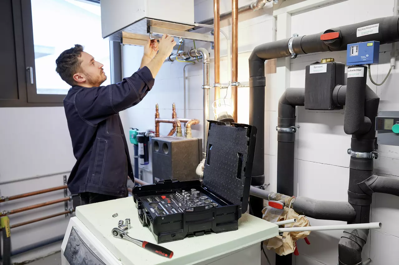 A person works on a ceiling unit with tools in a mechanical room