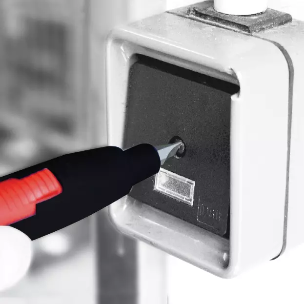 A hand holding a tool is operating a switch on a control panel.