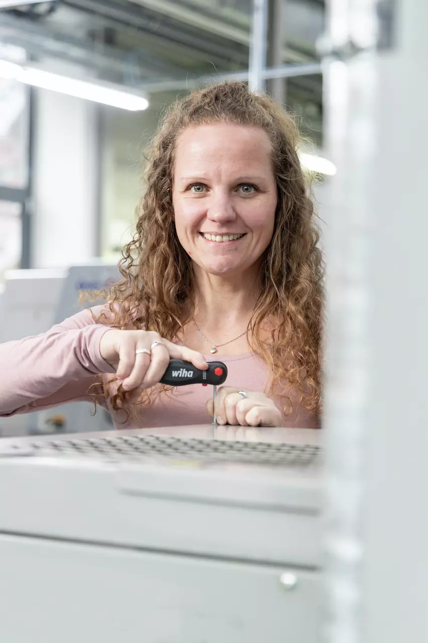 A woman using a black screwdriver on a metal grid.