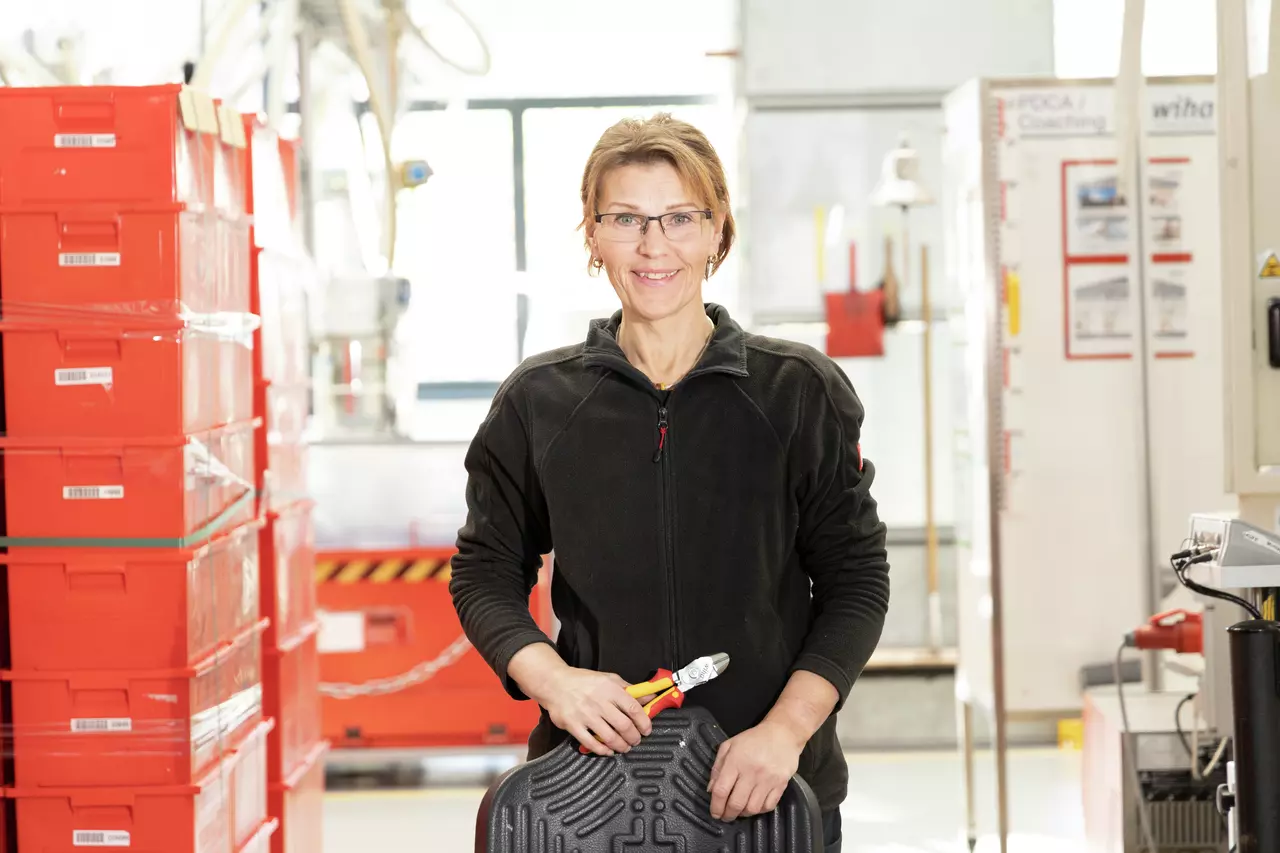 A person in work clothes holds an electric side cutter in a workshop.