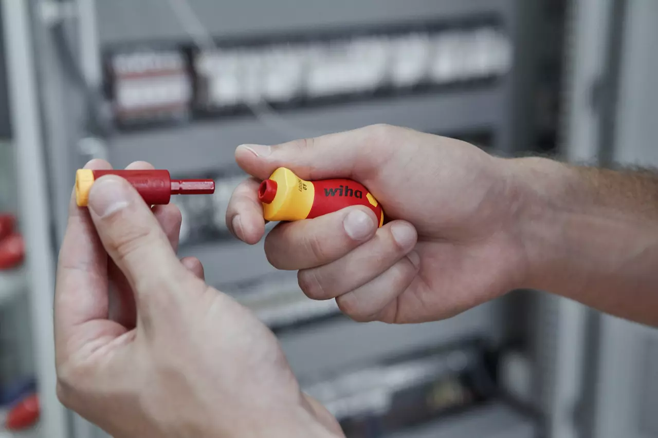 Hands holding an insulated bit and an electric screwdriver handle in red and yellow.