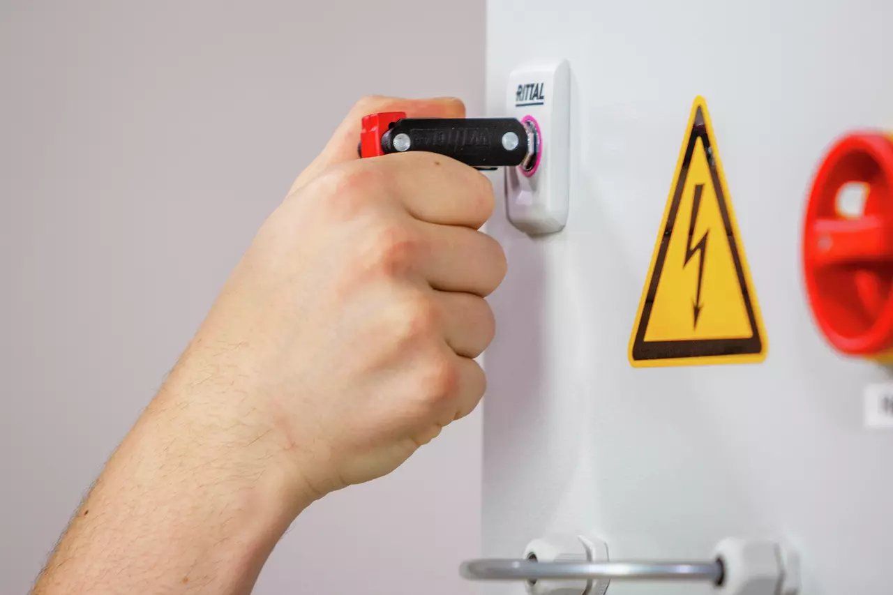 A hand using a universal key on an electrical panel with a high voltage warning sign.