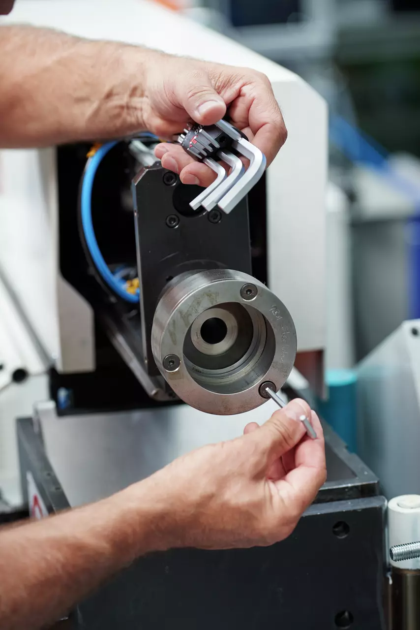 A person uses a hex key set to adjust a metal machine part.