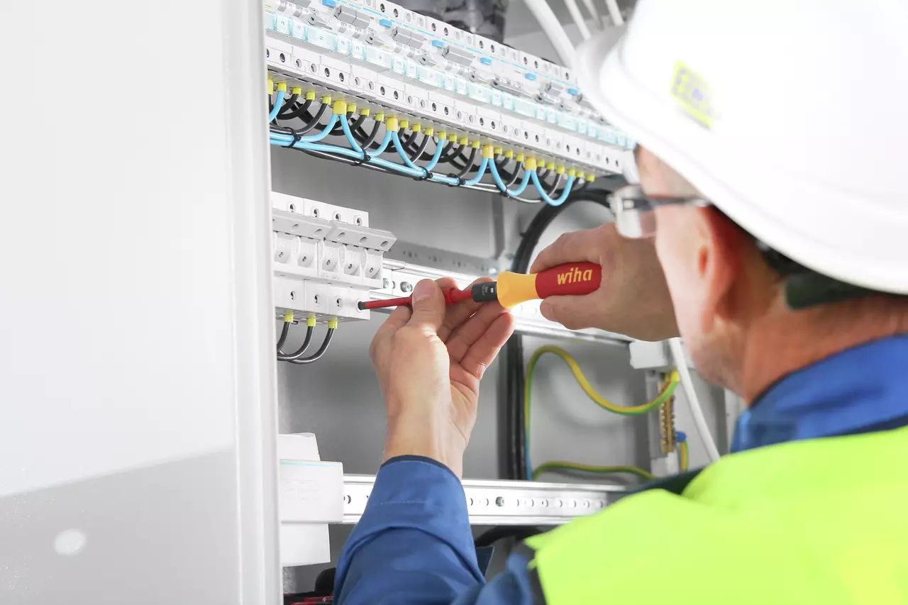 Person using an electric screwdriver on electrical panel