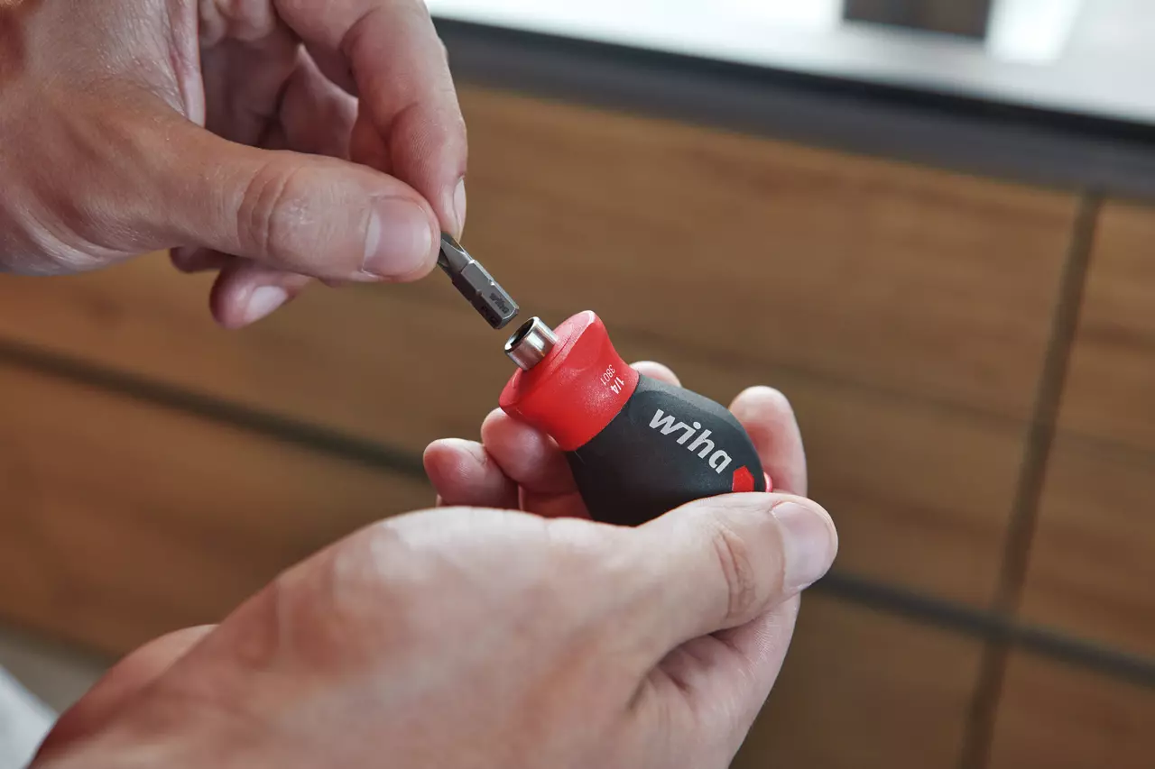 Person inserting a bit into a stubby screwdriver with a red and black handle.
